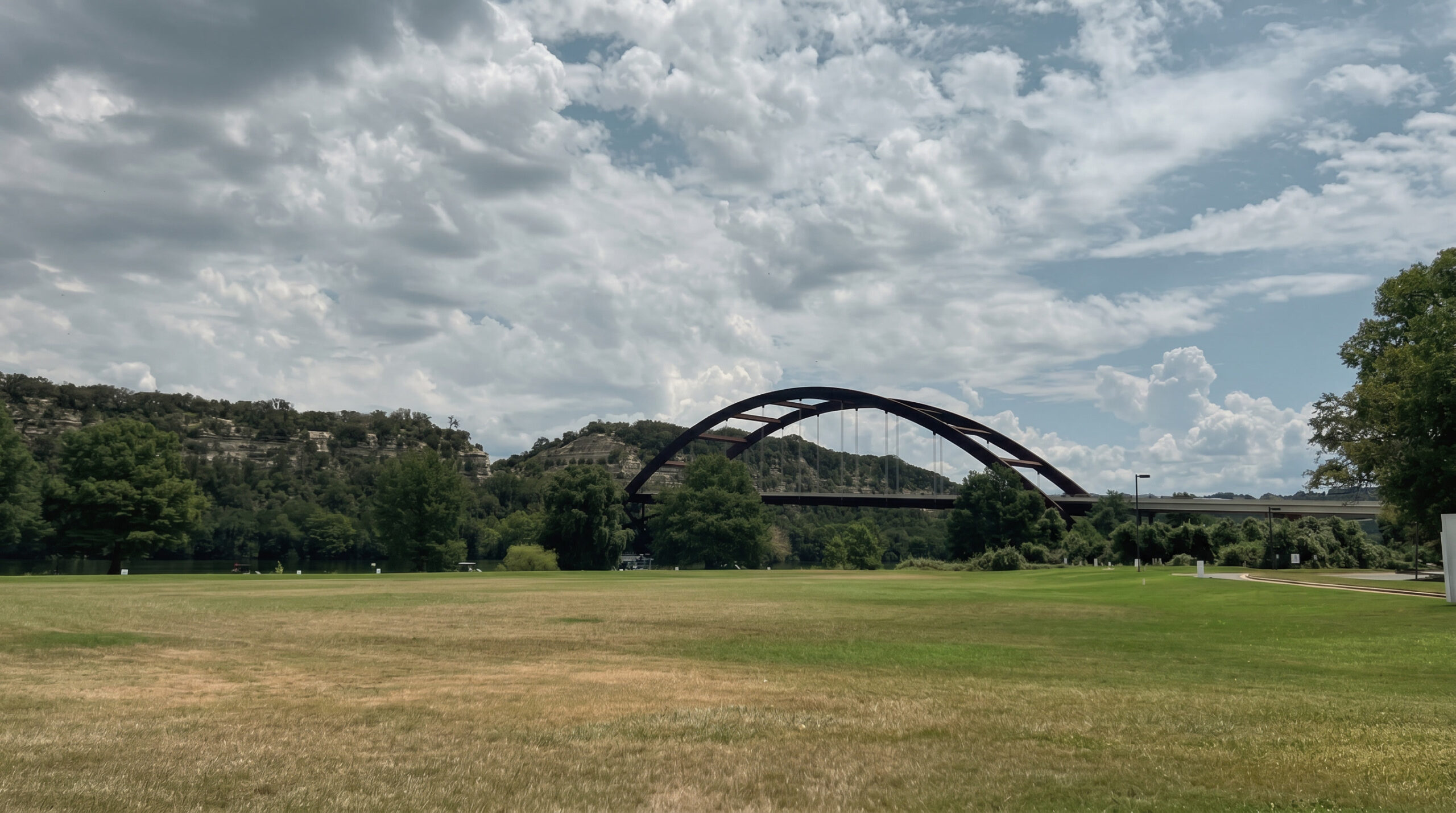 A reflective view of Pennybacker Bridge in Austin, Texas beneath dramatic clouds and worn grass, symbolizing pressure, resilience, and professional growth.