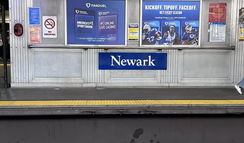 Newark Path Train Stop Newark PATH train station platform with sports betting advertisements and a bold blue Newark sign, capturing a quiet moment before heading into New York City — a scene that sets the tone for reflecting on bar exam mindset and personal growth.