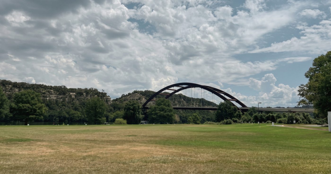 A reflective view of Pennybacker Bridge in Austin, Texas beneath dramatic clouds and worn grass, symbolizing pressure, resilience, and professional growth.